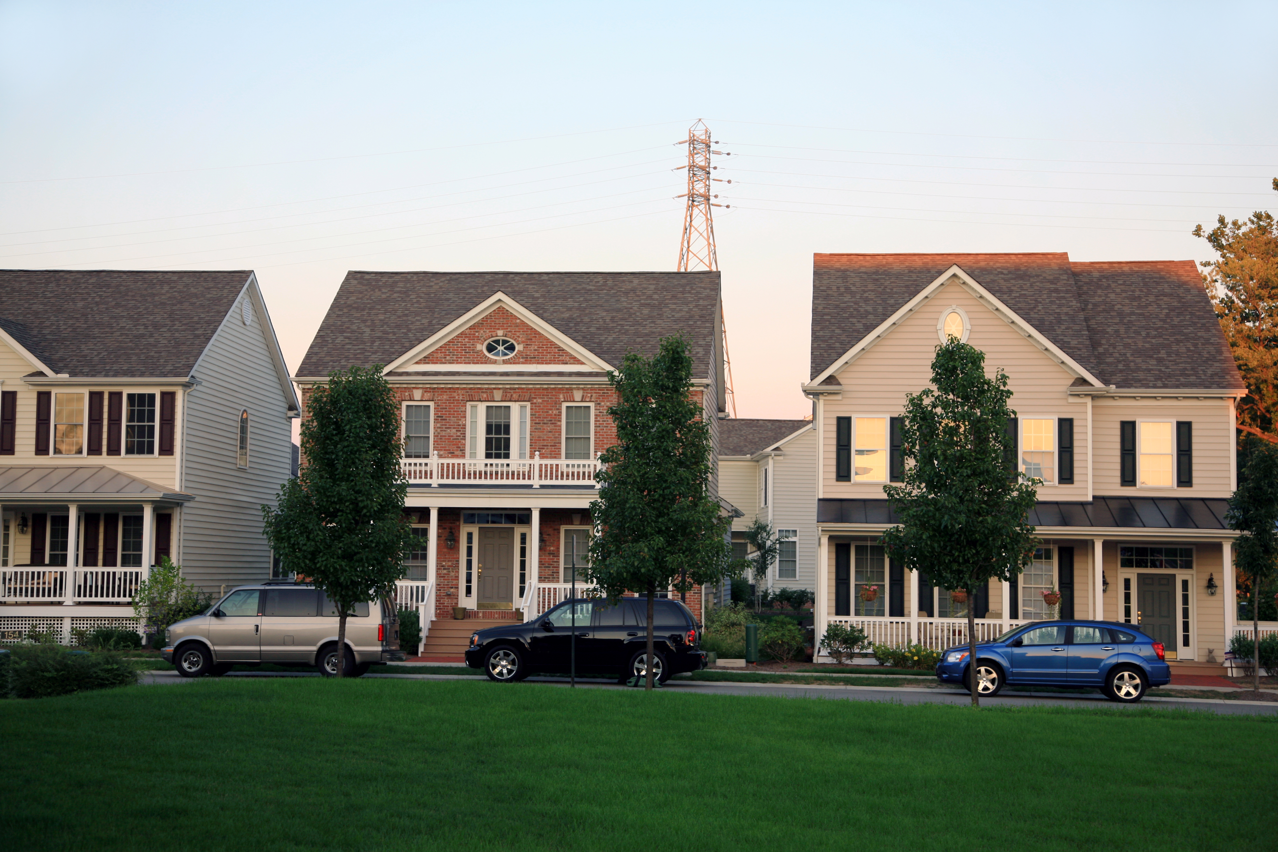A residential street with three houses side by side, three tress and three cars